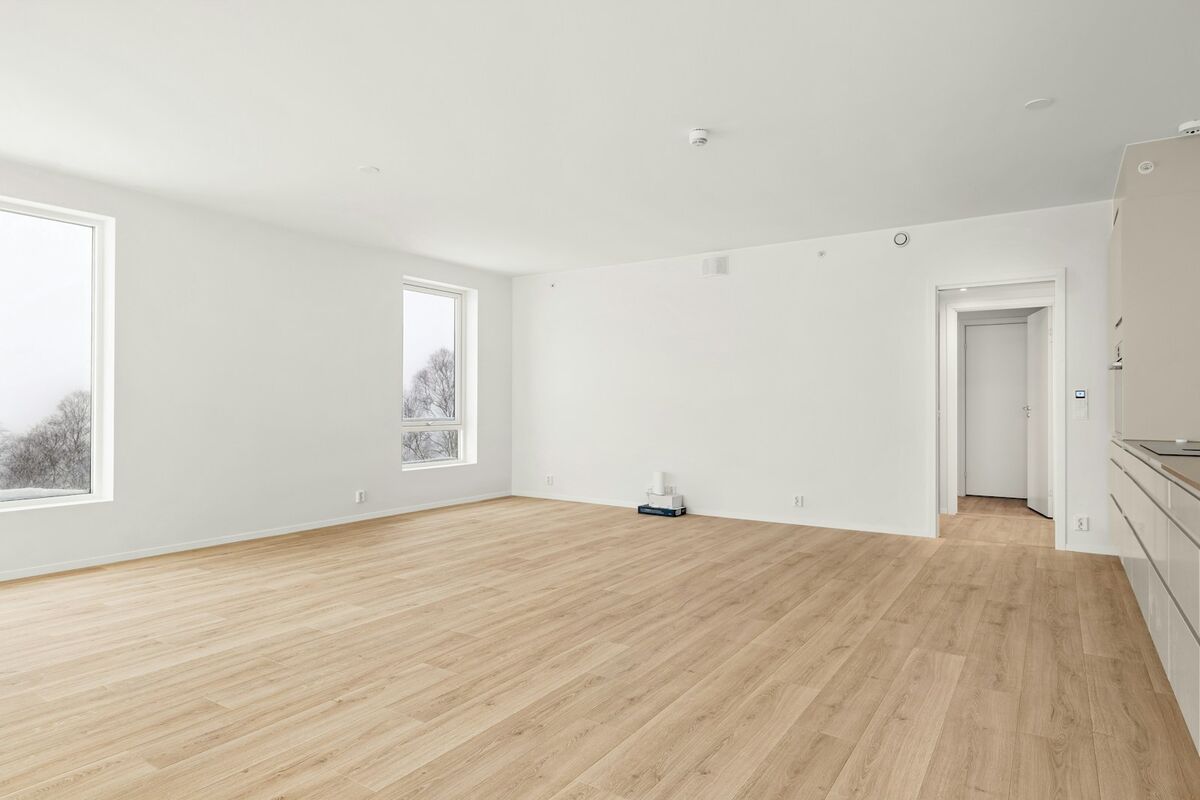A clean, empty living room with pale wood floors and natural light, ready for a new tenant.