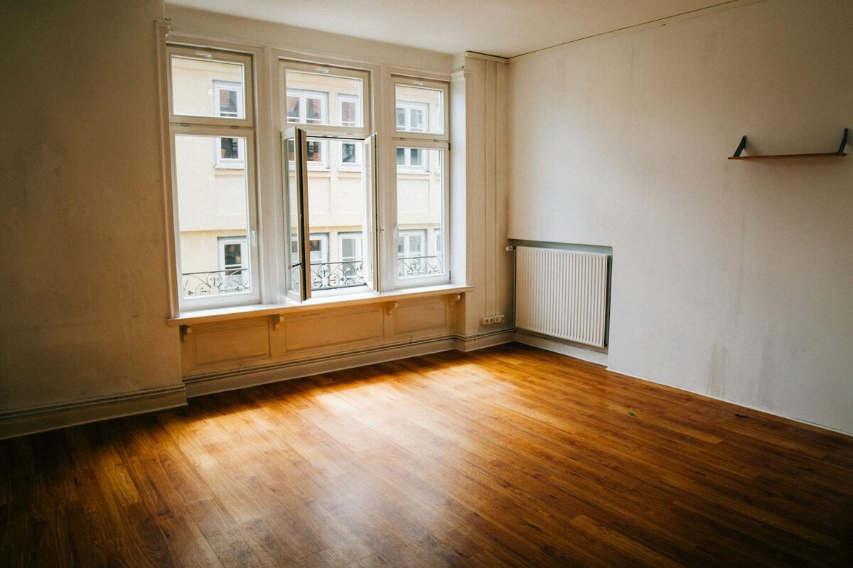 An empty room with polished wood flooring and tall windows.